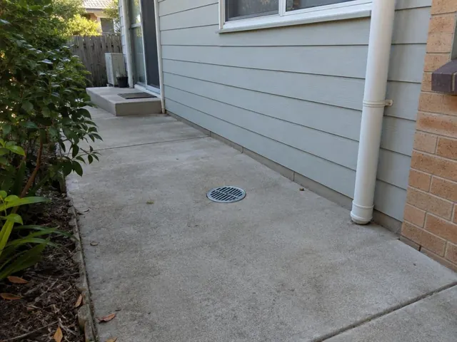 Dry concrete side path with a grated outdoor drain beside weatherboard walls in Allambie Heights