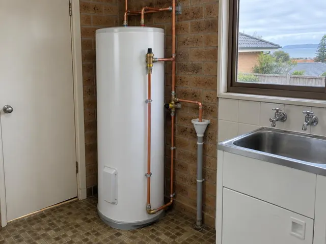 Hot water cylinder with copper pipework beside a laundry sink and window in Dee Why